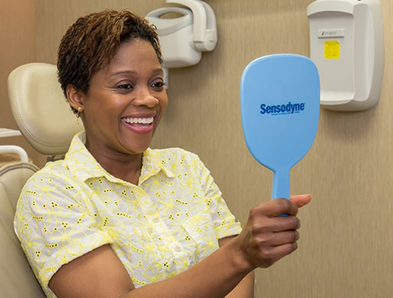 Woman holding a mirror and beaming at her smile after cosmetic dentistry in Port Chester