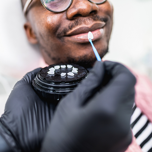Cosmetic dentist holding a veneer in front of a smiling patient