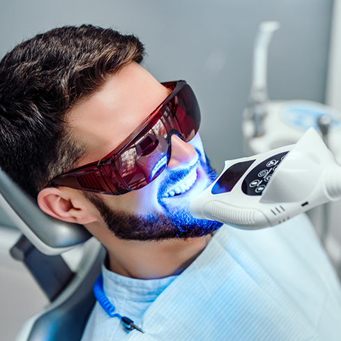 Man in the dental chair having a whitening light shone onto his teeth