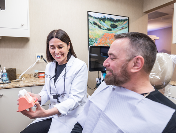 Dentist showing a patient a model of the mouth with dental implants in Port Chester