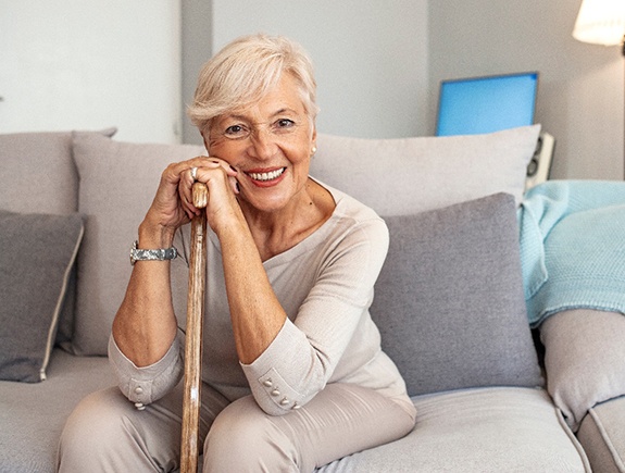 Woman in beige clothing on beige couch smiling leaning on walking cane