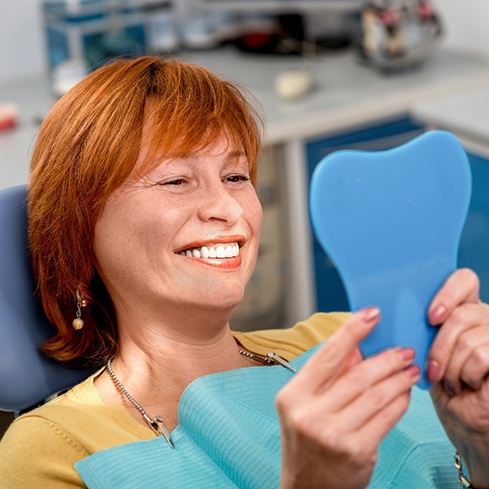 Woman with red hair in dental chair smiling at reflection in mirror