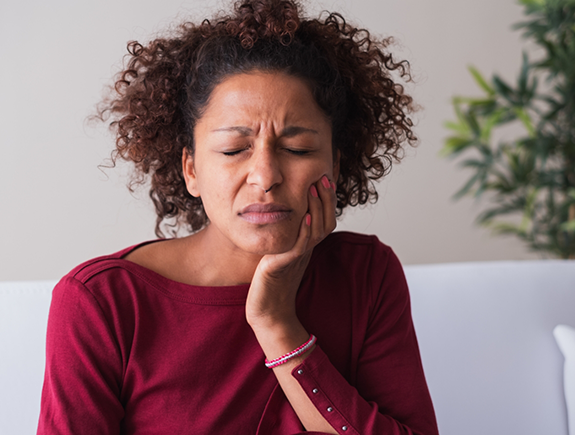 Woman holding her cheek in pain and needing an emergency dentist in Port Chester