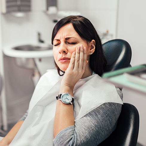 Woman sitting in the dental chair and holding her cheek in pain