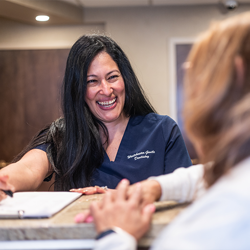 Smiling dental office receptionist handing a clipboard to a patient