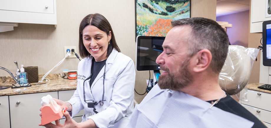 Port Chester dentist smiling as she shows a patient a model of the teeth