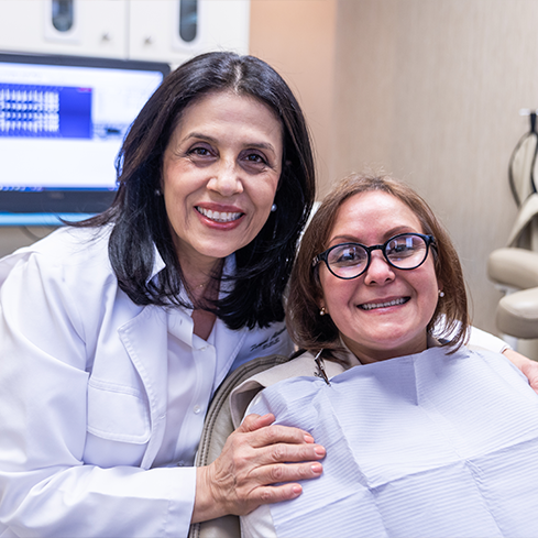Doctor Alidadi smiling next to a woman sitting in the dental chair