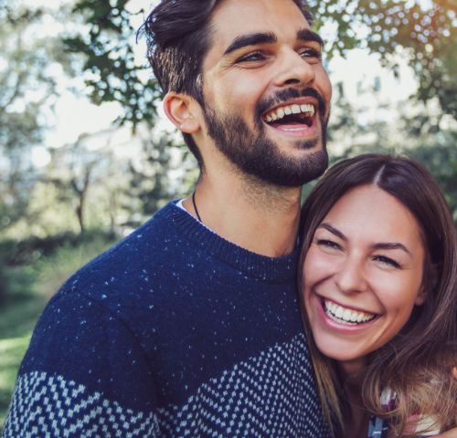 Young man and woman laughing while the man hugs the woman from behind