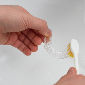 Patient using toothbrush to clean aligner