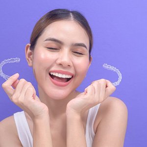 Woman holding Invisalign aligners and smiling