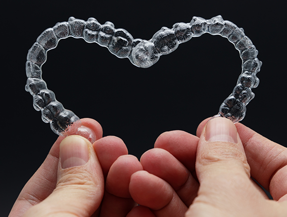 Hands holding two Invisalign clear aligners in the shape of a heart