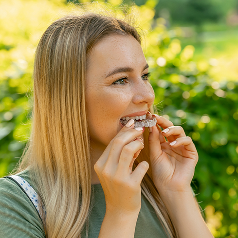 Young blonde woman placing an Invisalign aligner over her teeth