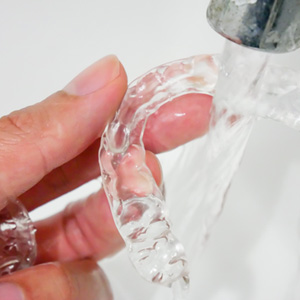 Patient rinsing clear aligner with water in sink