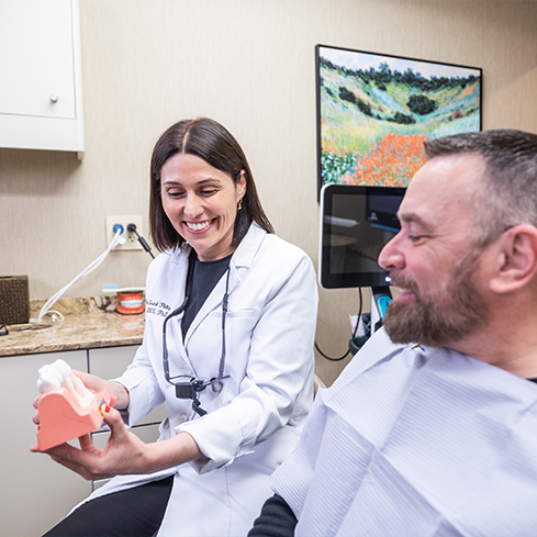 Doctor Pellegrini smiling while she shows a patient a model of the teeth