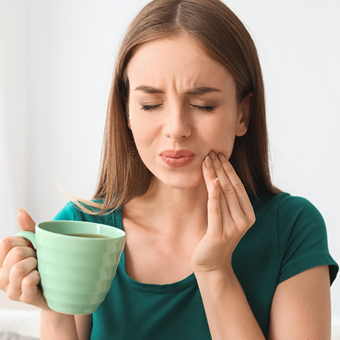 Woman holding a coffee mug and touching her cheek in pain